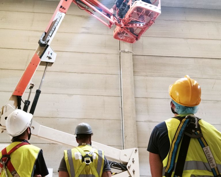 Empleados trabajando dentro de una nave industrial equipados con equipos de protección individual y arneses anticaída. 